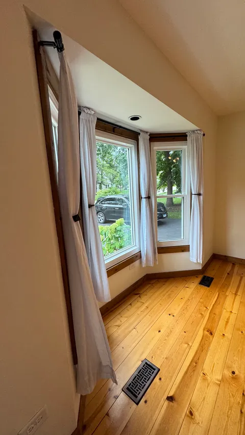 Bay window with fresh curtains above a mopped hardwood floor and clean floor vents