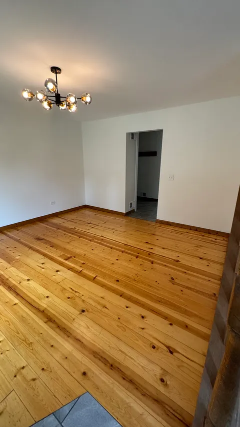Empty room with a swept pine floor and dusted chandelier after a move-out cleaning