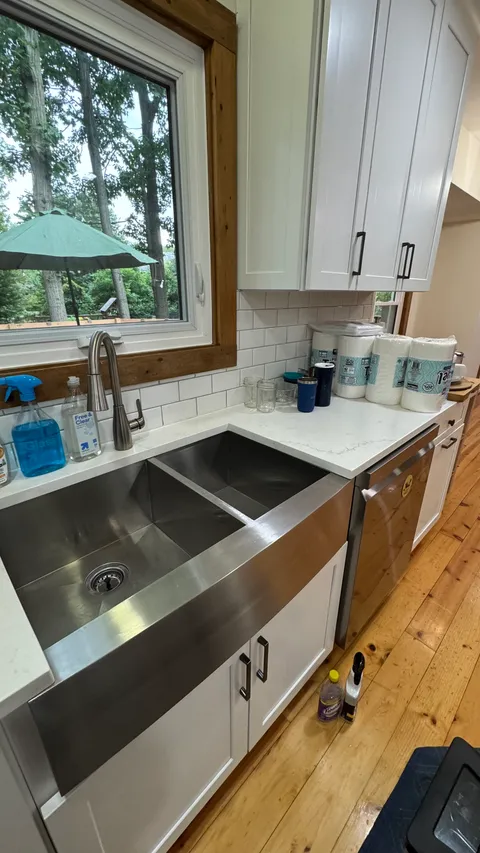 Polished stainless farmhouse sink and streak-free quartz counter by a kitchen window