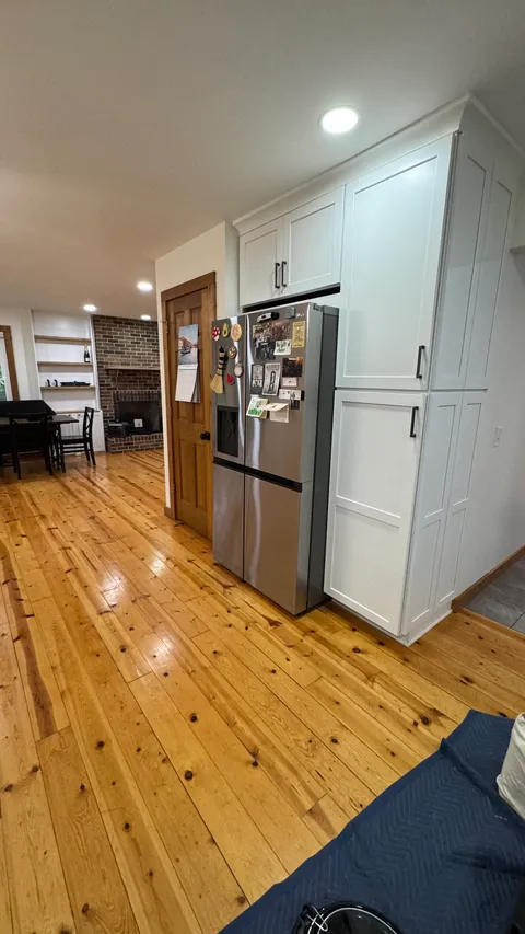 Mopped hardwood floor beside a stainless refrigerator and white pantry cabinets