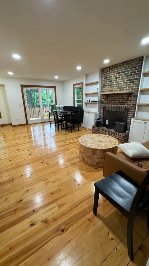 Living room with a brick fireplace, dusted shelving and gleaming hardwood floors