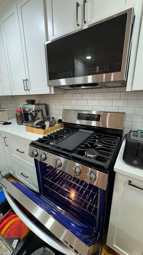 Cleaned stainless range and microwave hood below dusted white kitchen cabinets